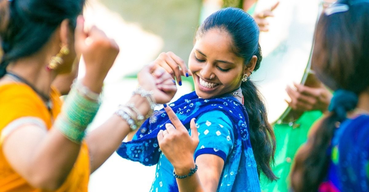 A young woman in a blue dupatta dancing and smiling