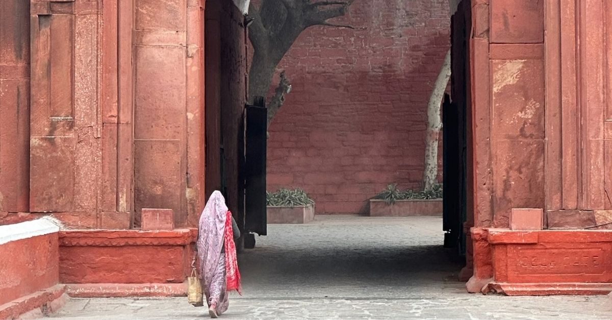 A woman in a sari walking through a red sandstone gateway in India